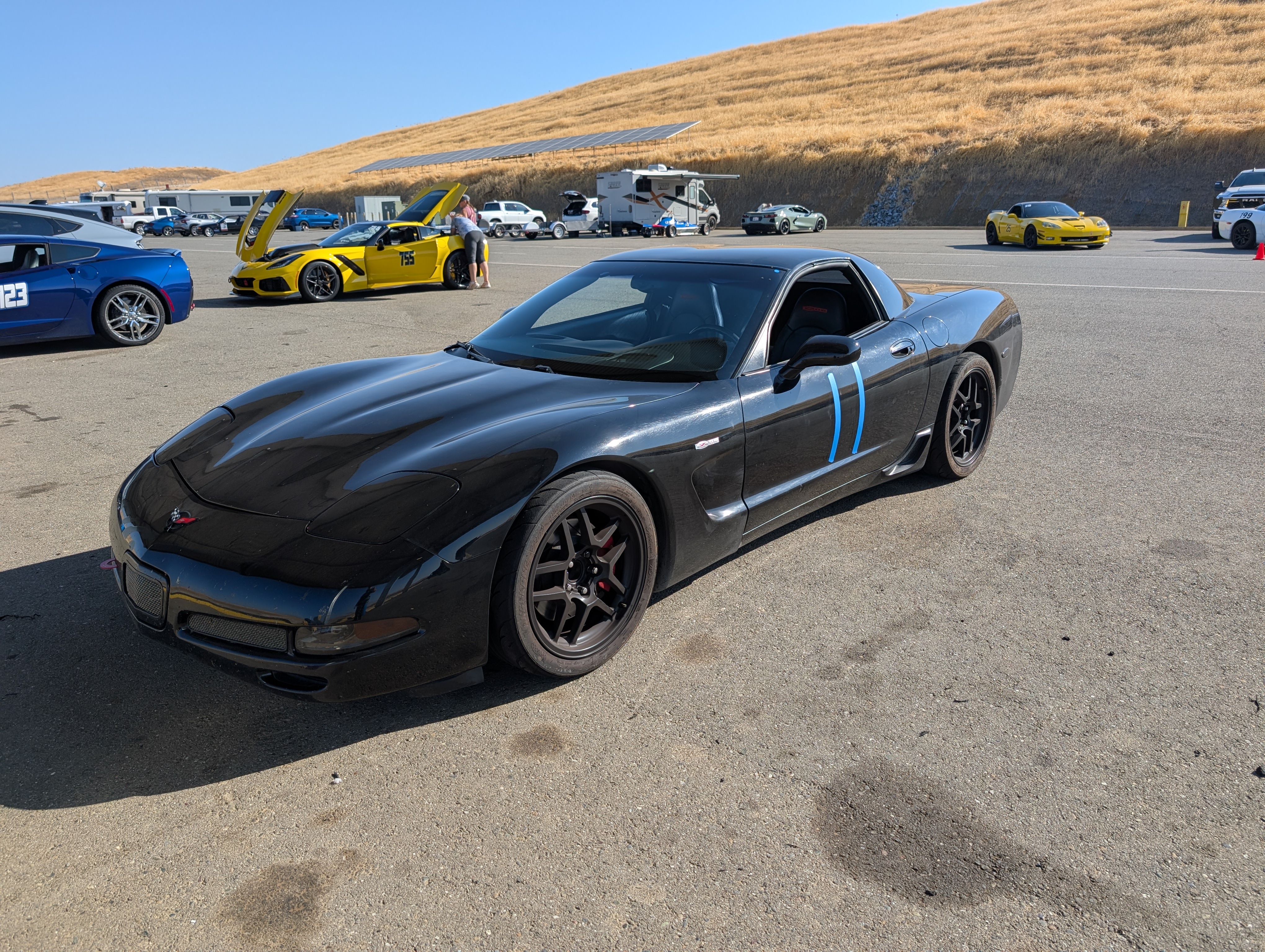 A black C5 Corvette #11 in the Paddock at Thunderhill West. Behind it are 4 more Corvettes as well, and a just barely the corner of a 5th one on the right side of the picture.