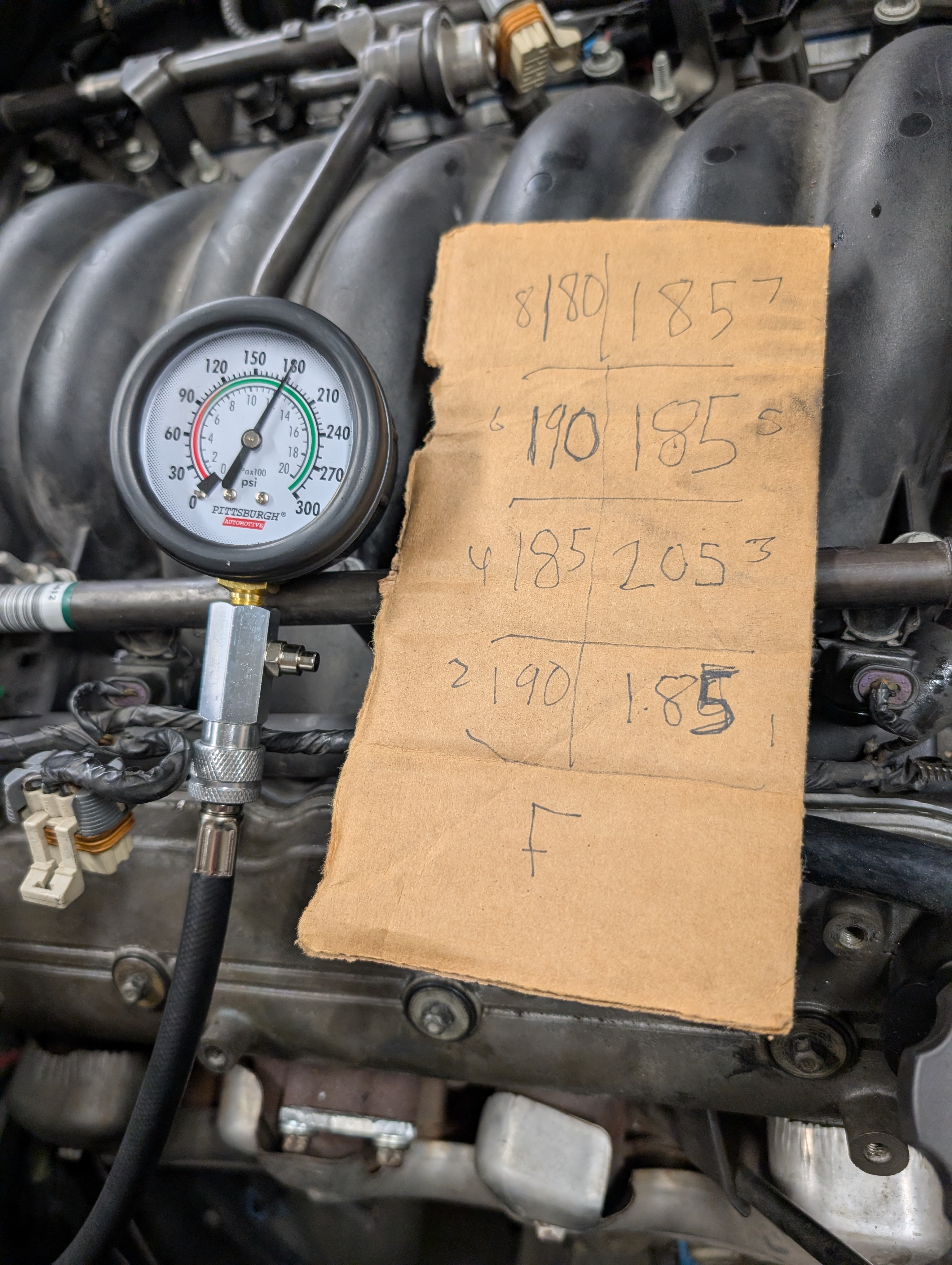 A compression tester laying on an LS1 next to a sheet showing good compression all around on the Dead to Shred LS1 motor