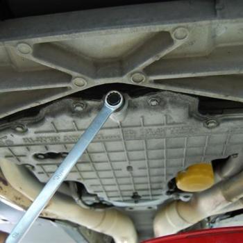 A C5 Corvette batwing oil pan, viewed from below in a C5 Corvette, with a box wrench on the oil drain bolt