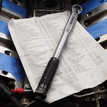 A picture of the torque values sheet printed out with a torque wrench ontop of it, all on the valley cover of an LS1 from a C5 Corvette
