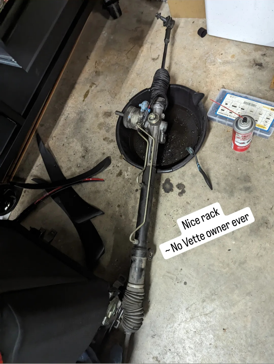 A C5 Corvette steering rock out of the car over a drain pan with the text "Nice Rack - No Vette owner ever"